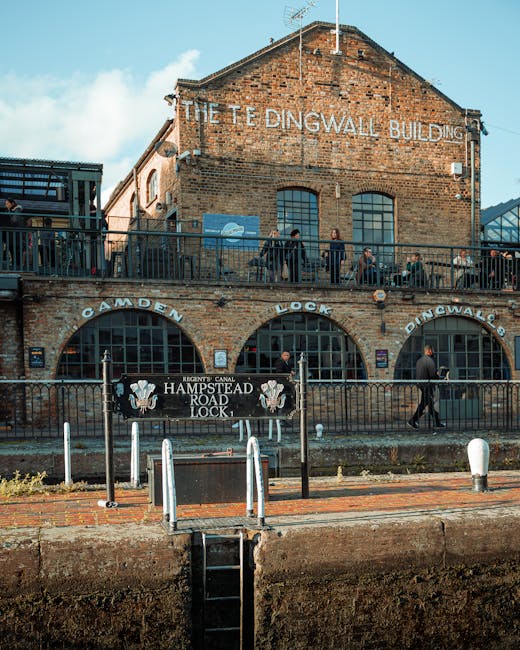 The image shows a historic brick building identified as 'The Tideingwall Building,' with weathered red-brown bricks and large arched windows on the lower level, enclosed by a black metal railing. Abov